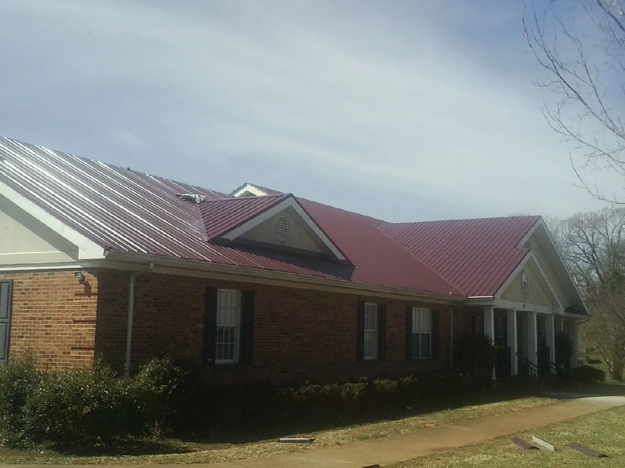 Red metal roof with gabled entries on a long brick building, from a Hail Damage Roof Repair job in Humboldt