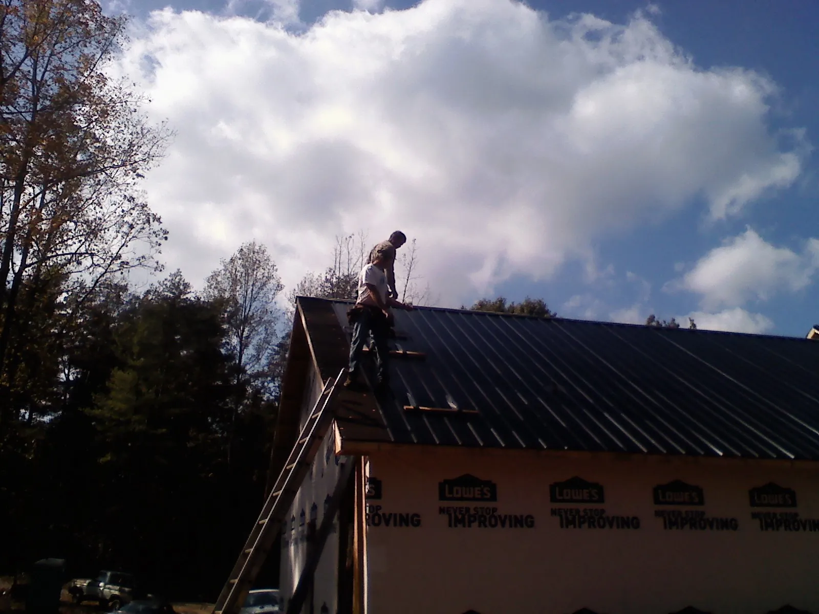 Roofer fastening dark metal panels high against a cloudy sky, from a Roof Inspection job in Humboldt